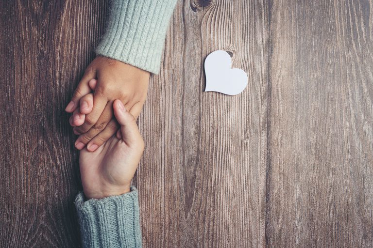 Two people holding hands together with love and warmth on wooden table